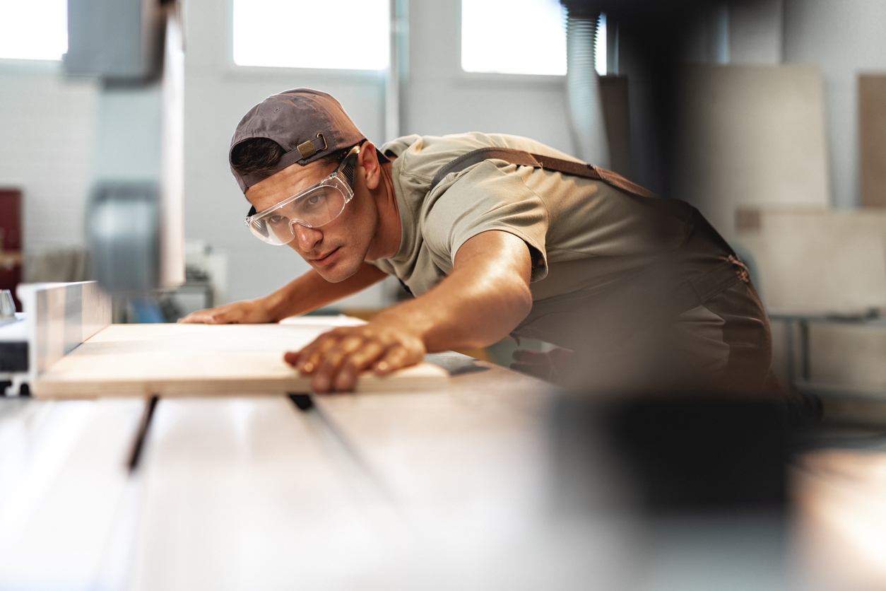 Young trades worker cutting a piece of wood in using a circular saw in furniture factory close up